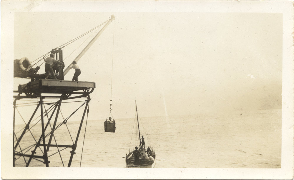 Man in the South Solitary Island crane basket moving into boat, 1930s