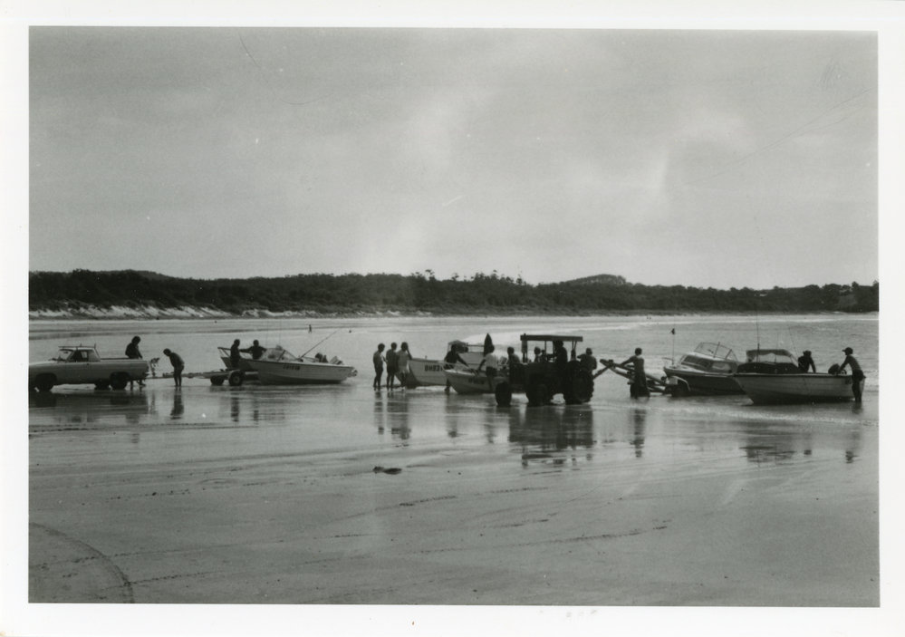 Fishermen and tractors hauling motorboats and boat trailers up Woolgoolga Beach