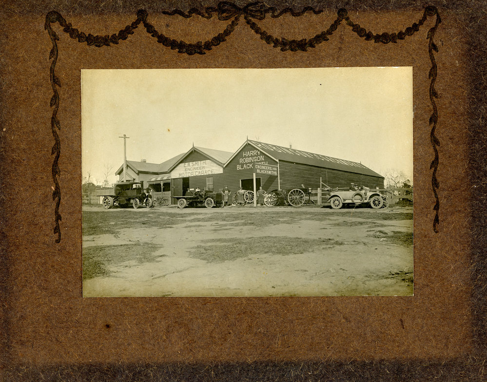 Cars and a motorised bicycle at the Harry Robinson and E W Smith workshops, c. 1920