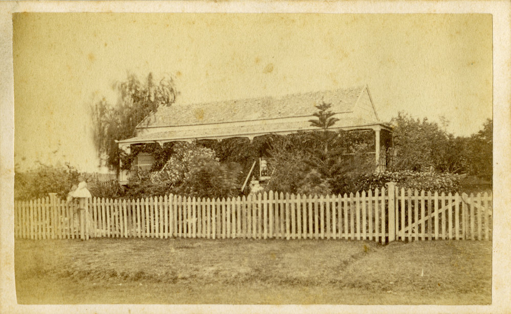 A woman and three children standing in front of a house, c. 1870