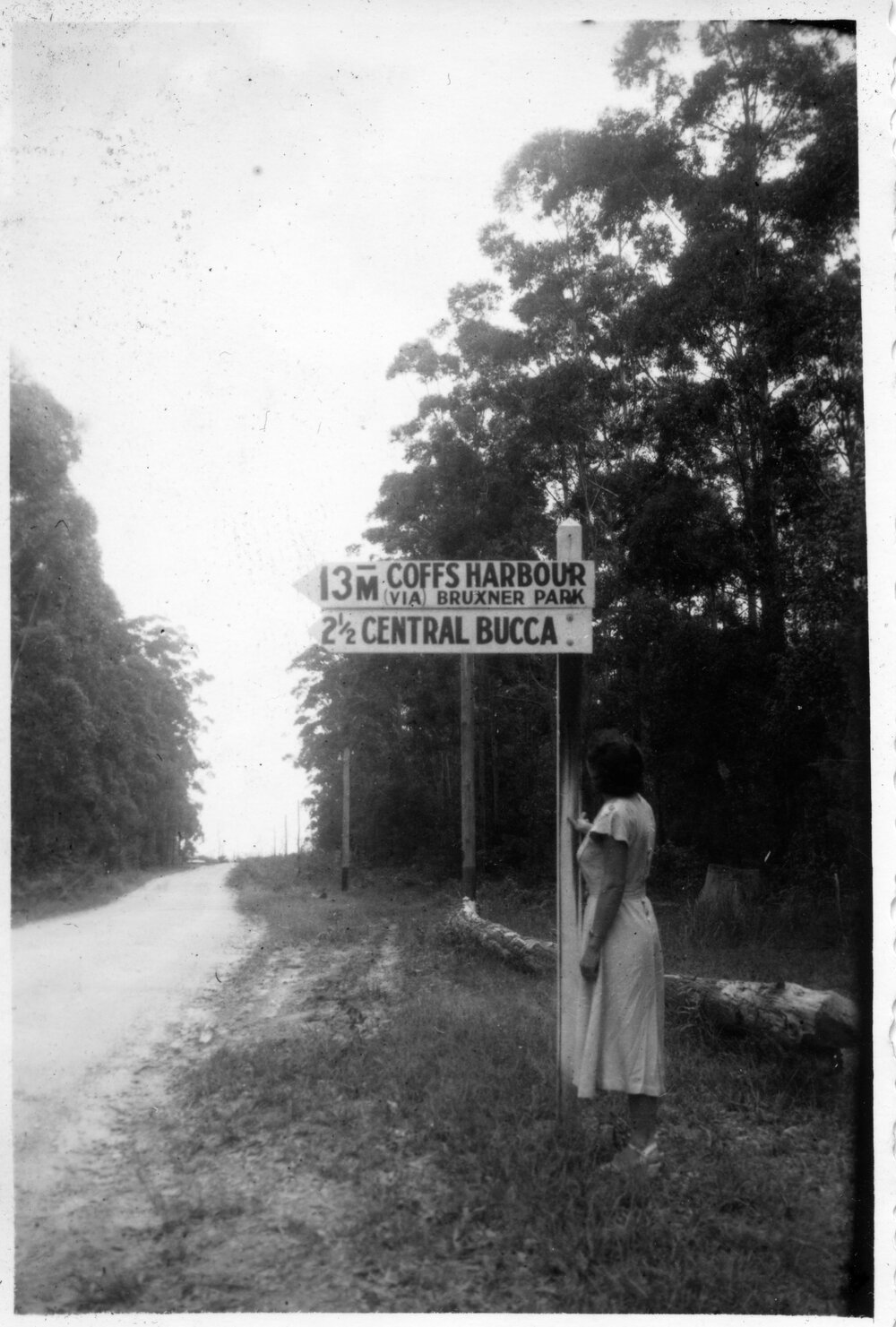 Ivy standing by the road sign 13 miles from Coffs Harbour, c.1955