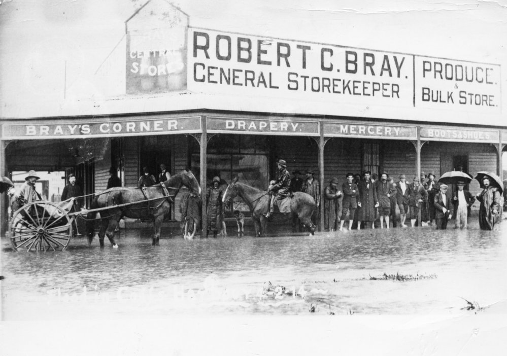 People standing in flood waters outside Bray's General Store on the corner of High and Moonee Streets, 4 February 1914
