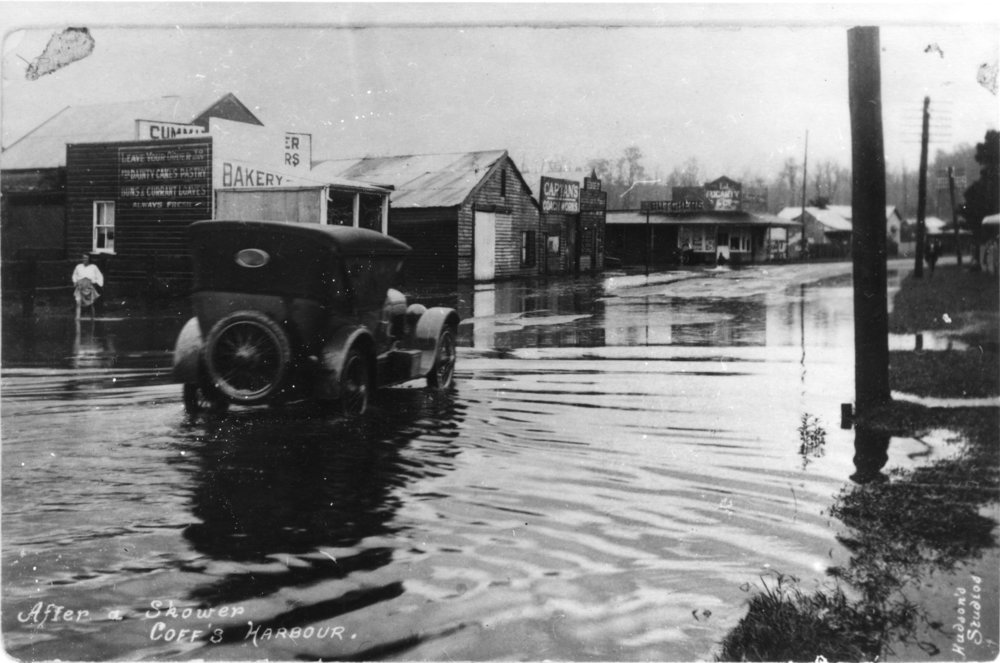 A car drives by the corner of West High Street and Lyster Street in flood waters after rain, c. 1922 