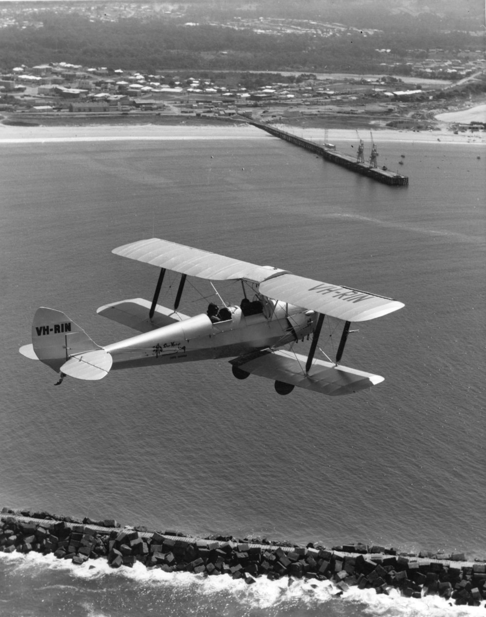 An aerial view of a Tiger Moth biplane VH-RIN flying over the Harbour, 1972