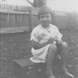 Heather McLeod sitting on her school case, c.1930