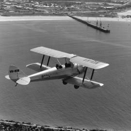 An aerial view of a Tiger Moth biplane VH-RIN flying over the Harbour, 1972