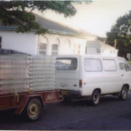 White van towing a trailer with crates, 1970s