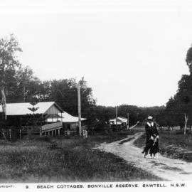 Ethel Bailey walks her dog past the beach cottages at Bonville Reserve, 1930s