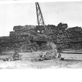 Stockpile of cut sleepers and uncut logs at Coffs Harbour Jetty for transport to New Zealand, early 1900s