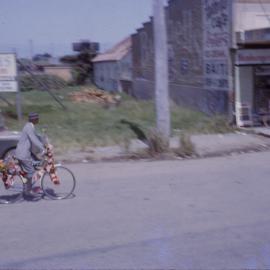 Cyclist on his decorated bicycle in a street parade at the Jetty strip, 1964