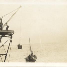 Man in the South Solitary Island crane basket moving into boat, 1930s