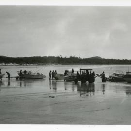 Fishermen and tractors hauling motorboats and boat trailers up Woolgoolga Beach