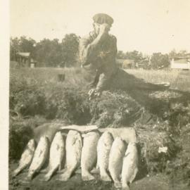 Fisherman with 8 fish on bank of river. Red Rock 1950