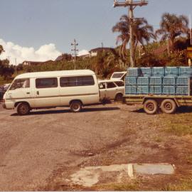 White transit van towing a trailer with crates, April 1982